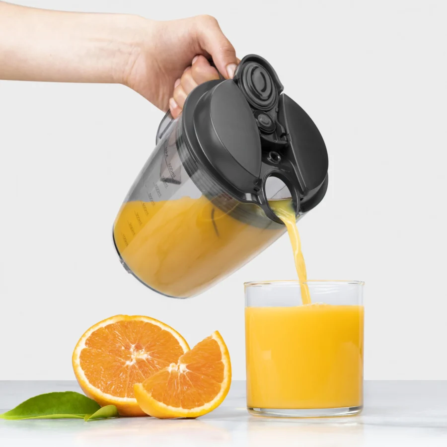 Mano sujetando el asa de la jarra de la nutribullet® Juicer 800W sirviendo jugo de naranja en un vaso sobre fondo blanco