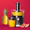 Extractor de jugos nutribullet® Juicer 800W con su tazón lleno de jugo, acompañado de piña y toronjas sobre fondo rojo