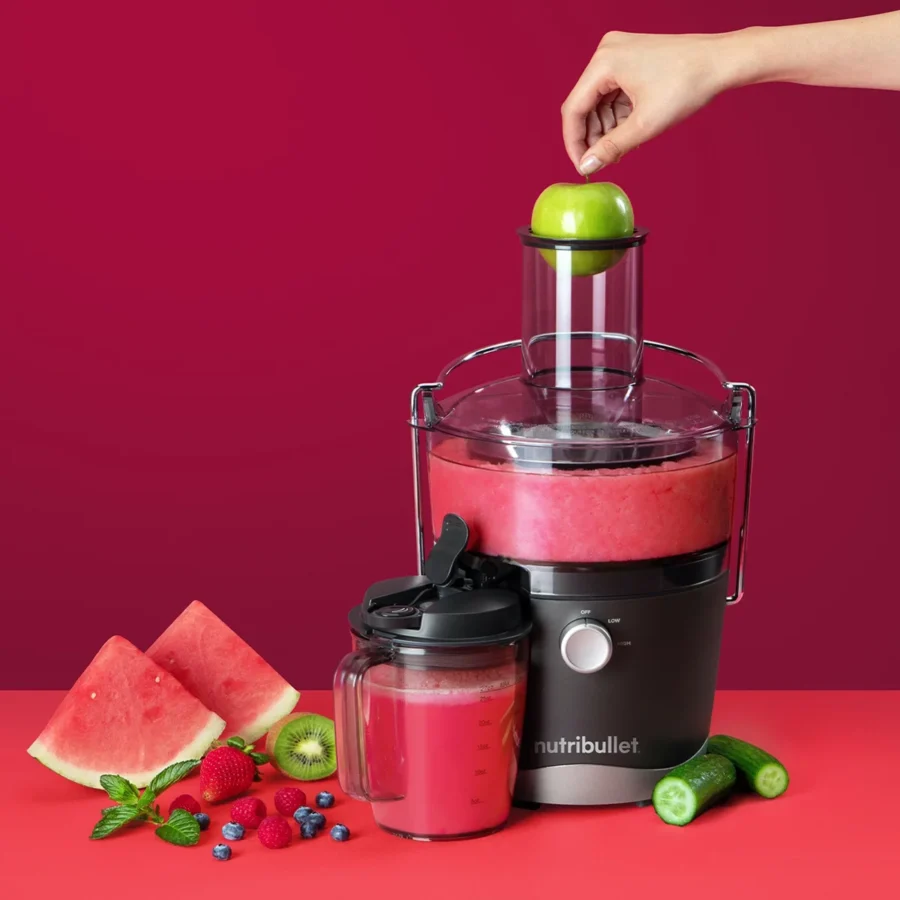 Extractor de jugos nutribullet® Juicer 800W con su tazón lleno de jugo, acompañado de trozos de sandía, fresas, kiwi y manzana sobre fondo rojo