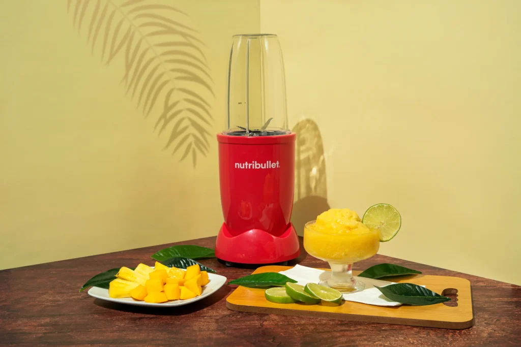 Sorbete Tropical, una nutribullet® 600W Rubí de la Colección Glossy junto con pedazos de frutas cortadas y una copa con el sorbete