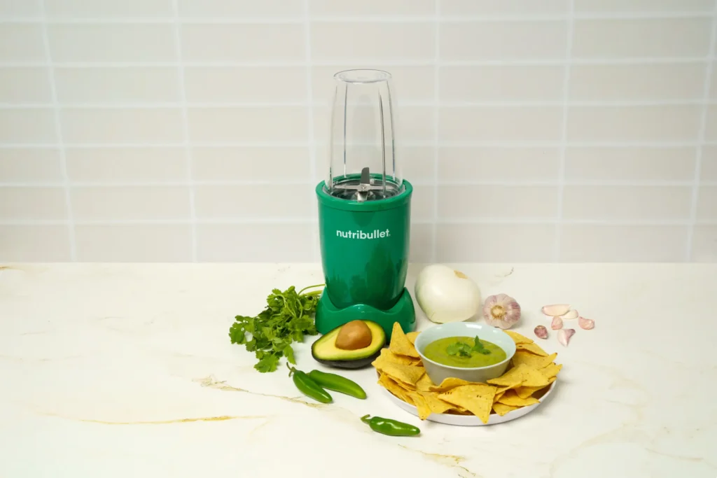 Salsa Verde, una nutribullet® 600W Esmeralda de la Colección Glossy, ingredientes en la mesa y un tazón lleno de salsa