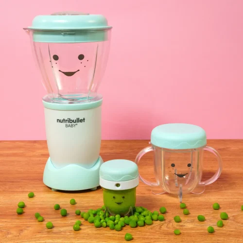 nutribullet® Baby con sus accesorios sobre una mesa, con el contenedor de guardado lleno de puré de chícharo