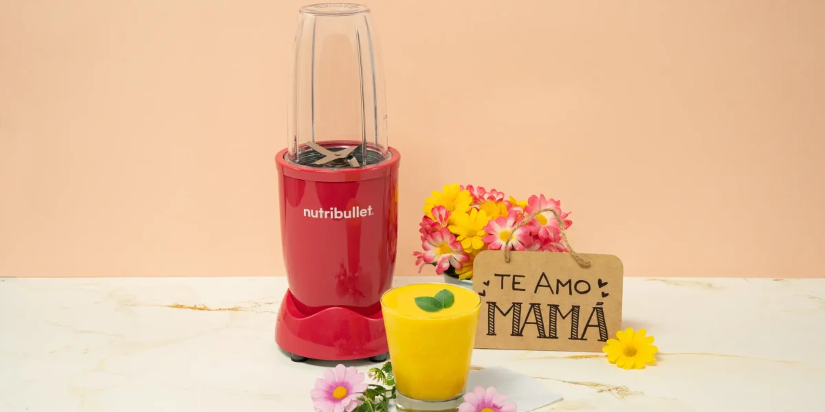 Smoothie Sunshine para mamá, una nutribullet® 600W Rubí de la Colección Glossy junto con flores, un letrero que dice ‘Te amo, Mamá’ y un vaso del smoothie