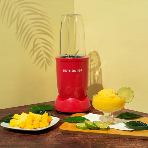 Sorbete Tropical, una nutribullet® 600W Rubí de la Colección Glossy junto con pedazos de frutas cortadas y una copa con el sorbete