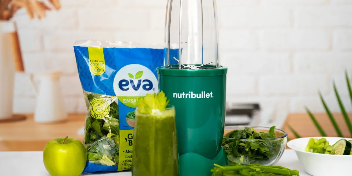 Jugo Verde con Ensalada EVA Green Boost, bolsa de ensalada EVA lista para comer junto a una nutribullet® 600W Esmeralda de la Colección Glossy, frutas y verduras de la receta, y un vaso del jugo final