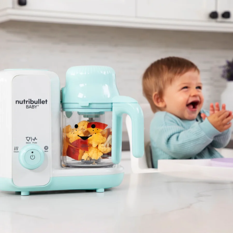 nutribullet® Baby Steam & Blend en primer plano, con un bebé riendo sentado en su silla para comer en el fondo