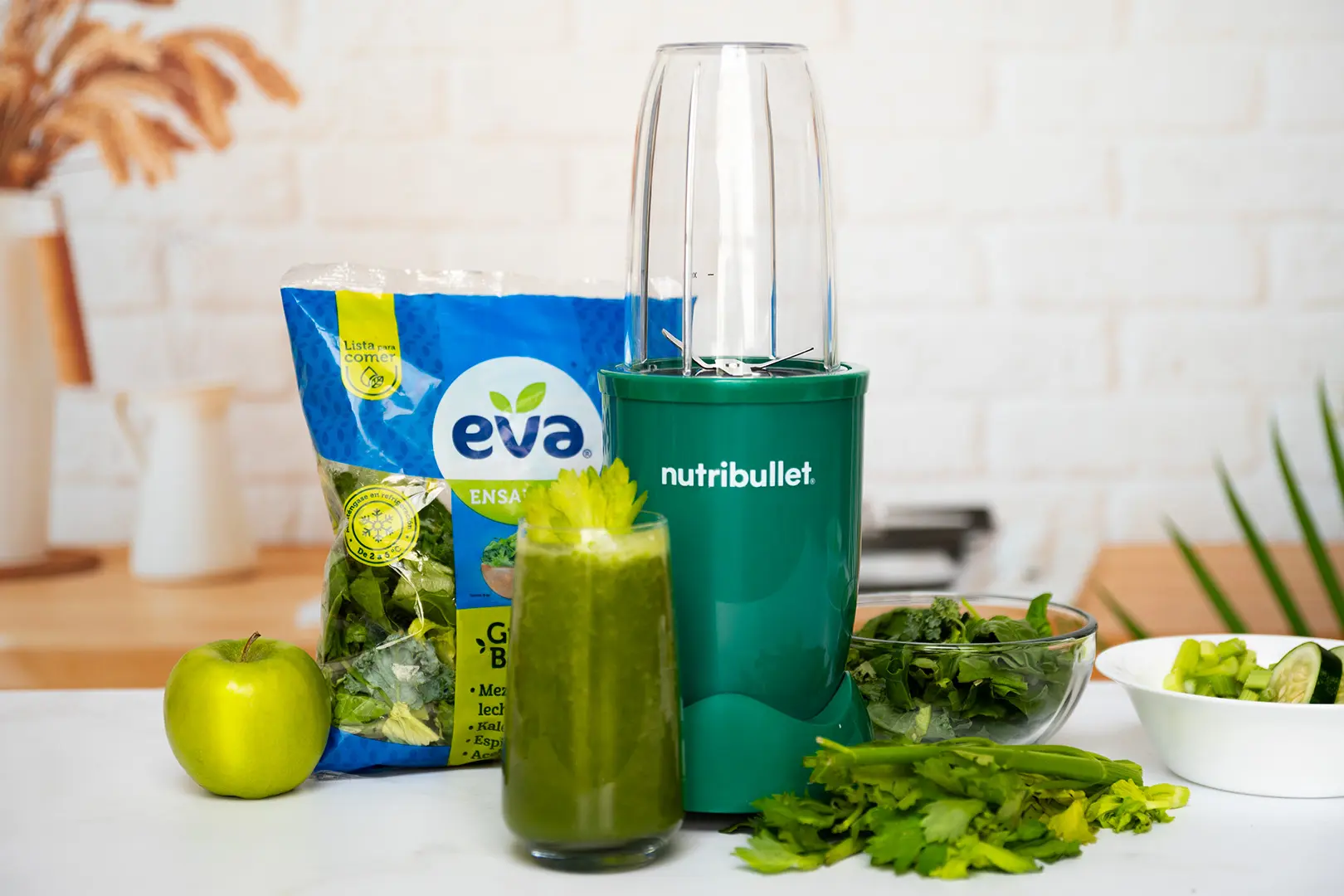 Jugo Verde con Ensalada EVA Green Boost, bolsa de ensalada EVA lista para comer junto a una nutribullet® 600W Esmeralda de la Colección Glossy, frutas y verduras de la receta, y un vaso del jugo final